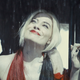 Margot Robbie's Harley Quinn looks up and appreciates the rain while wearing a bright red dress.